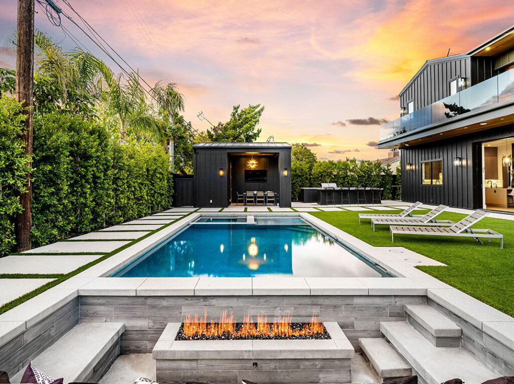 A contemporary swimming pool featuring a fire pit and lounge chairs in a residential outdoor setting.
