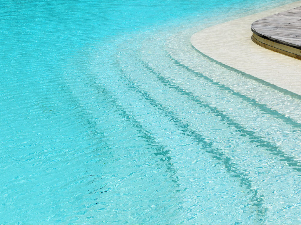 Clear turquoise water with a gradual beach entry and wooden decking on the side.